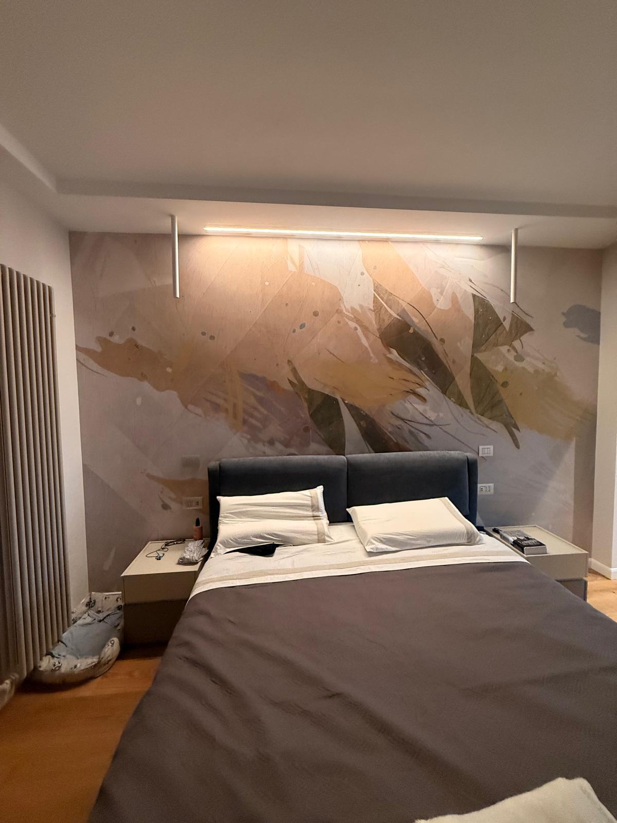 Camera da letto con parete decorata e profili luminosi a soffitto.